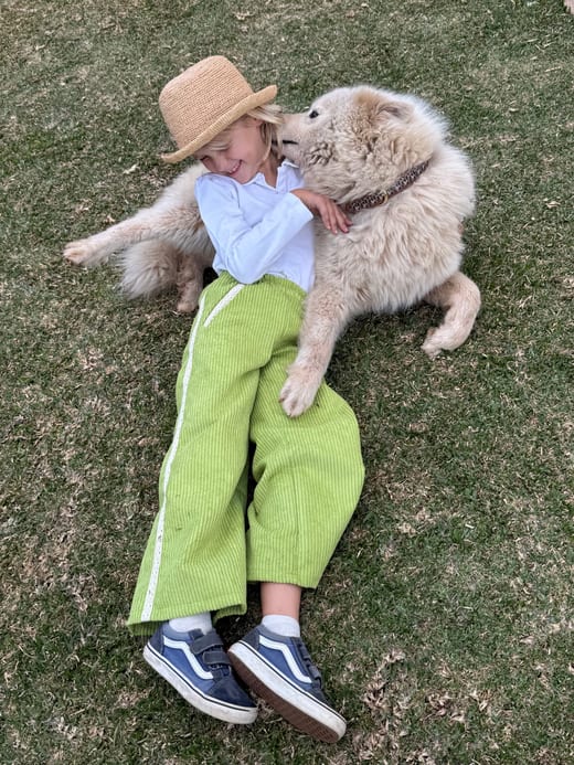 Enfant portant le pantalon Maitso vert anis, allongé dans l'herbe avec un chien